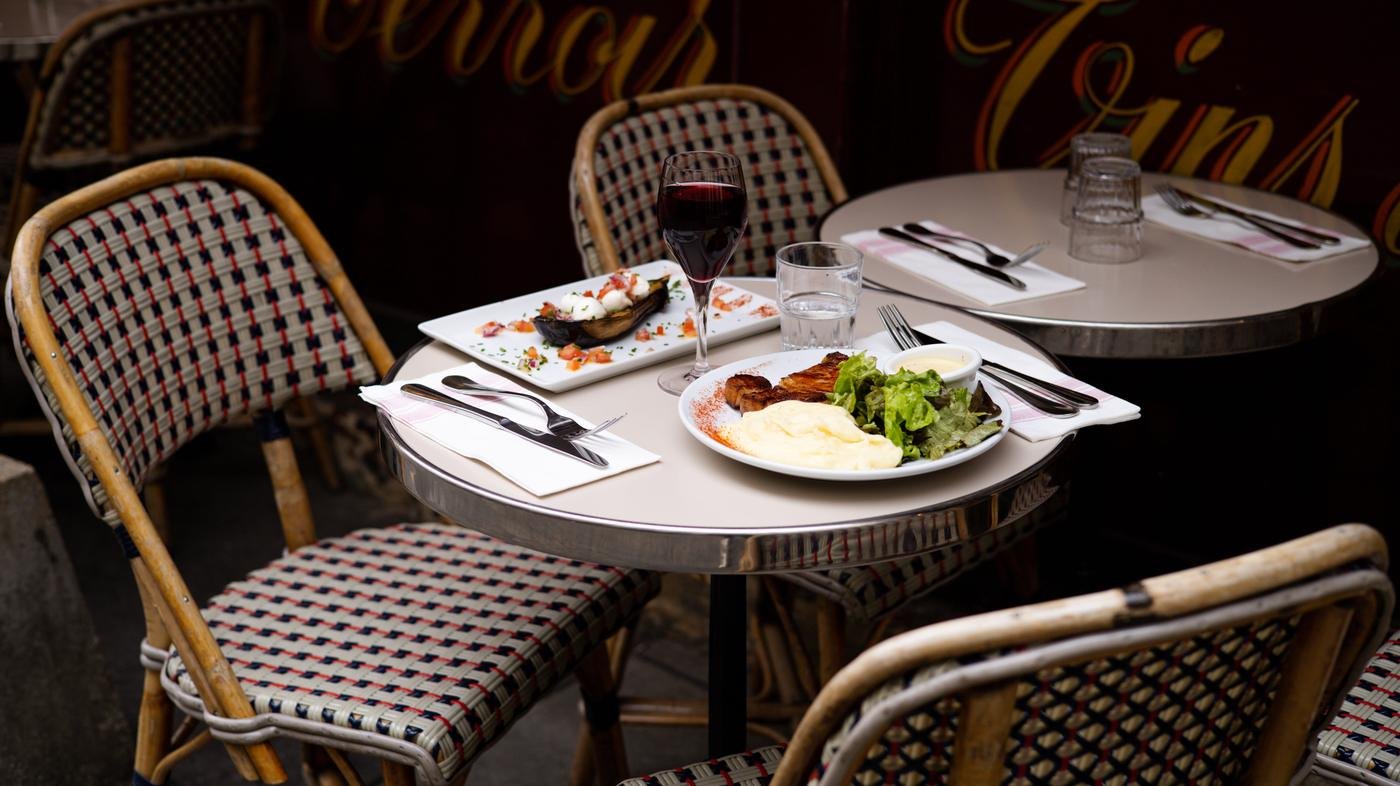 La salle du Lou Cantou : tables bistrot, chaises cannées et lettres dorées sur les vitres